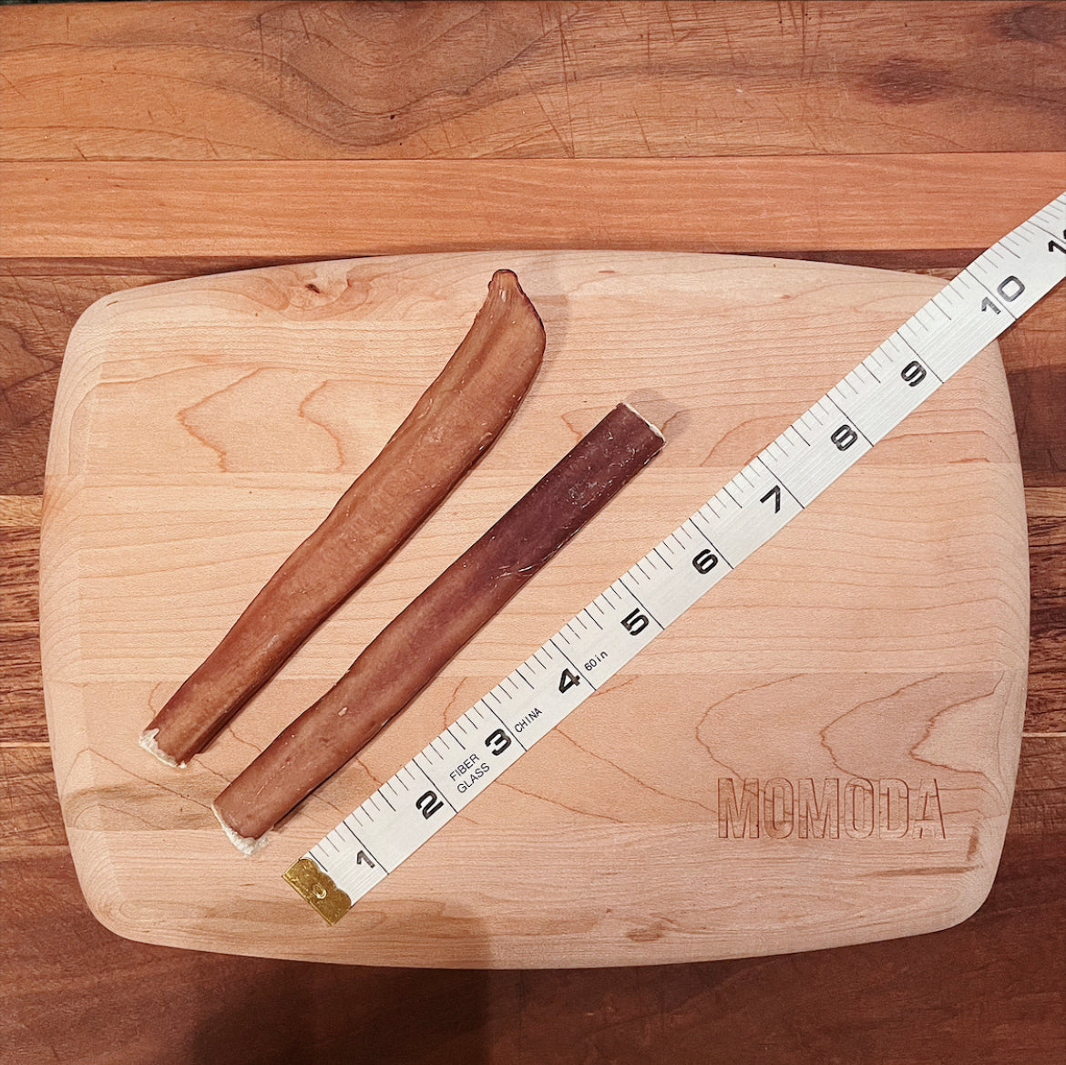 2 of the 6 inches bully sticks on a cutting board alongside a measuring tape showing the bully sticks are between 6 to 7 inches.