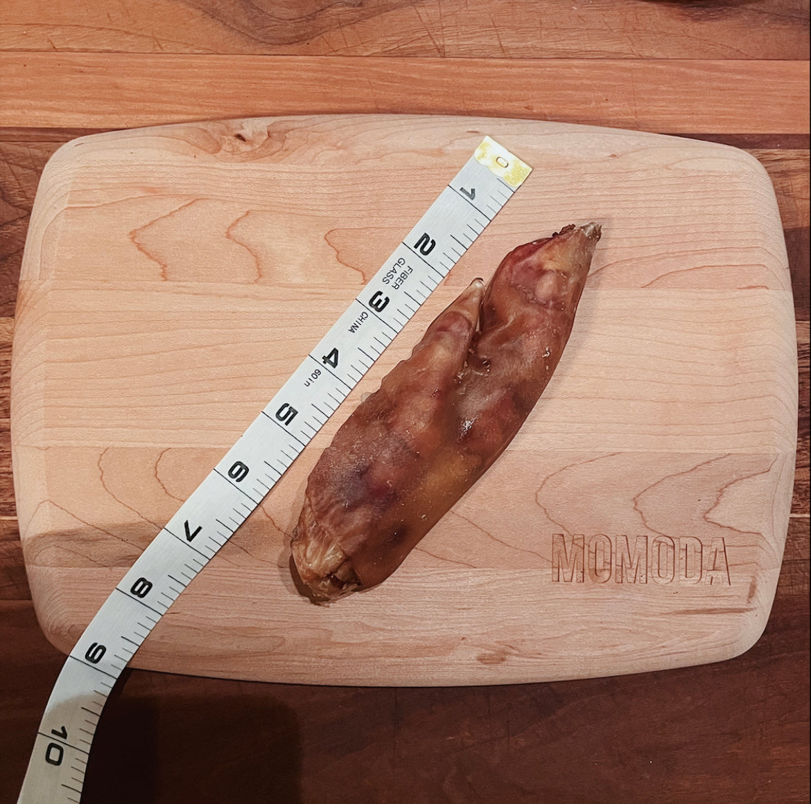 one piece of the pig trotter on top of the cutting board, alongside the measuring tape showing the pig trotter is between 6 to 7 inches.